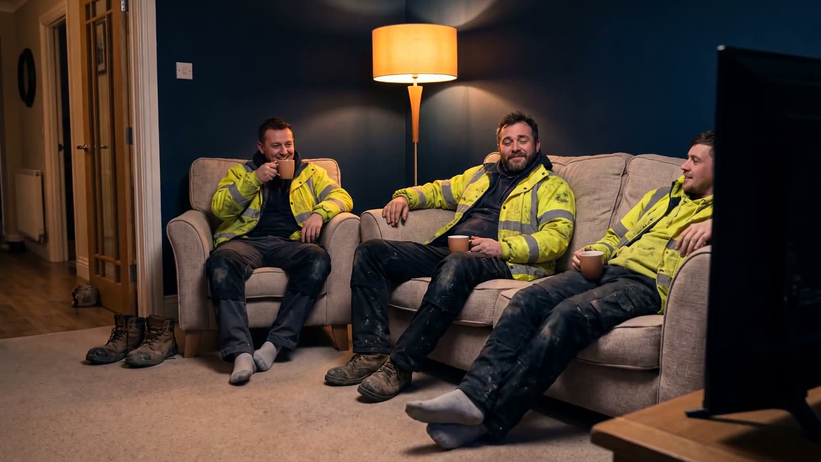 Construction crew relaxing with tea in an Overnightly house after a shift, boots off at the door